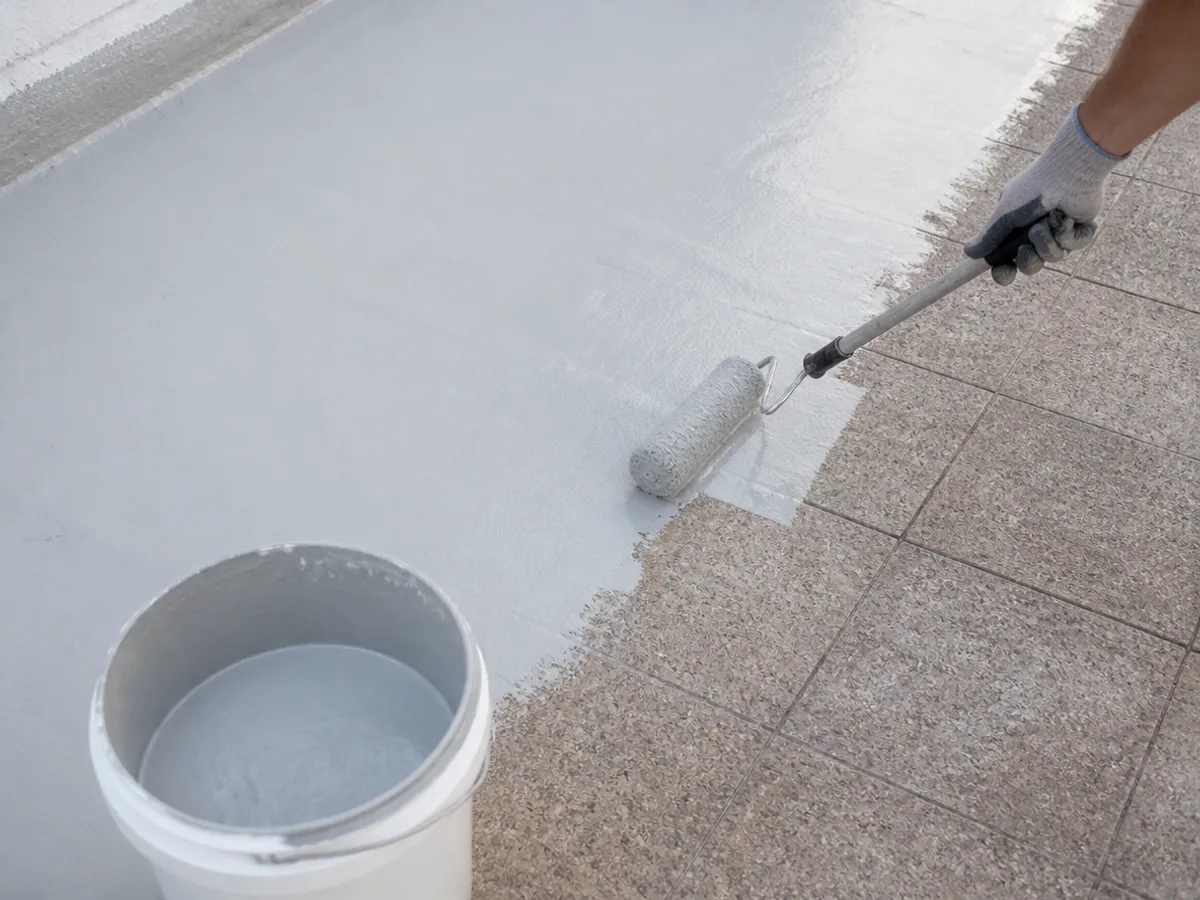 Rodillo extendiendo pintura de caucho gris claro sobre el suelo de una terraza a medio pintar